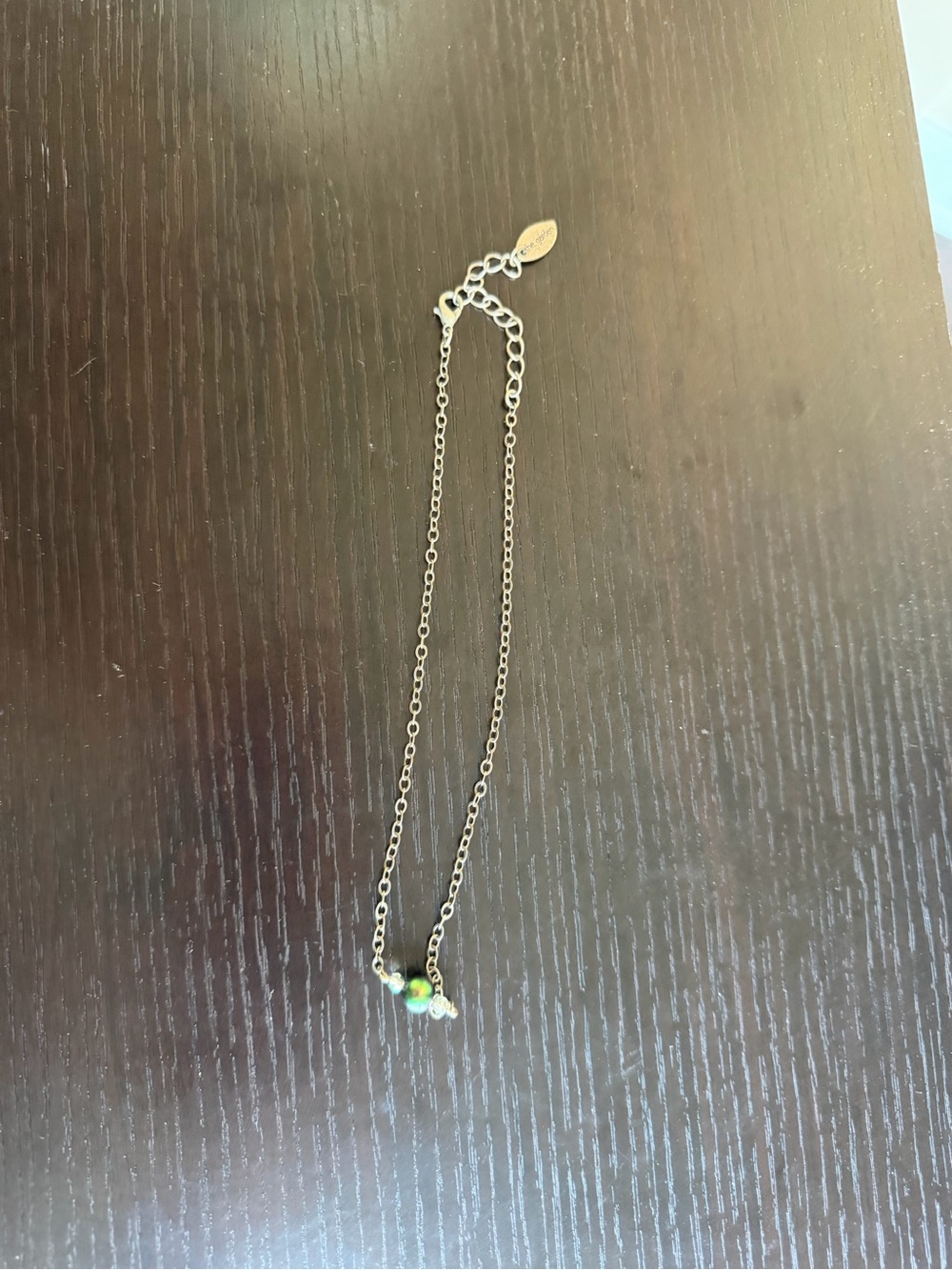 Silver-tone necklace featuring a round green bead and two smaller clear beads